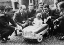 Damon Hill sitting in a toy car at his christening watched by some great names