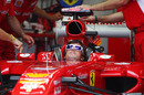 Fernando Alonso relaxes in his car as mechanics work on the Ferrari