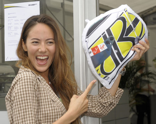 Jessica Michibata smiles while showing off a Jenson Button helmet-style cushion 