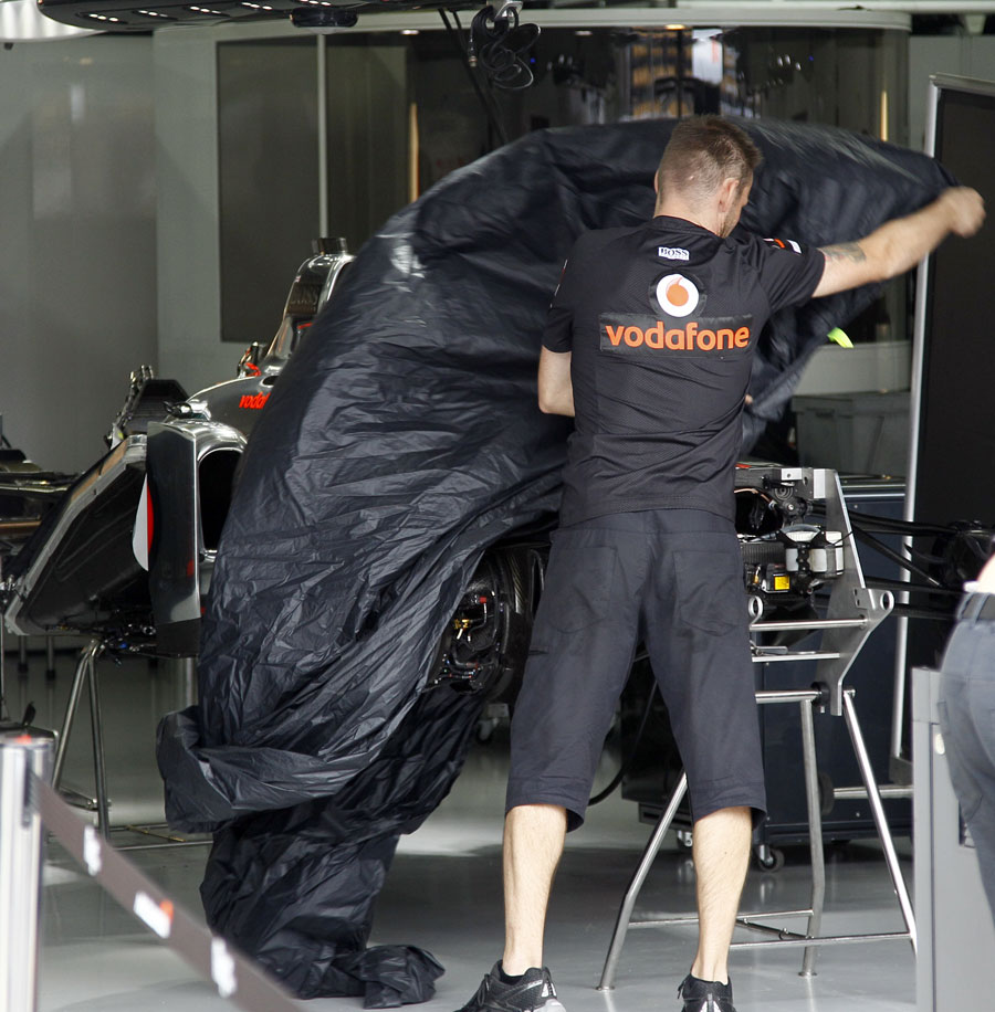 A McLaren mechanic covers up a chassis in the garage