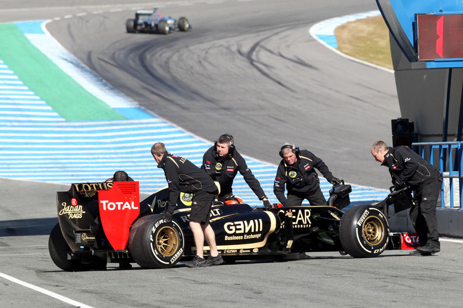 Kimi Raikkonen is wheeled back in the the Lotus garage as Michael Schumacher rounds turn one