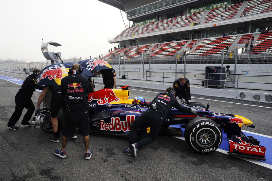 Sebastian Vettel is wheeled back in to the garage as Red Bull mechanics cover the car with umbrellas