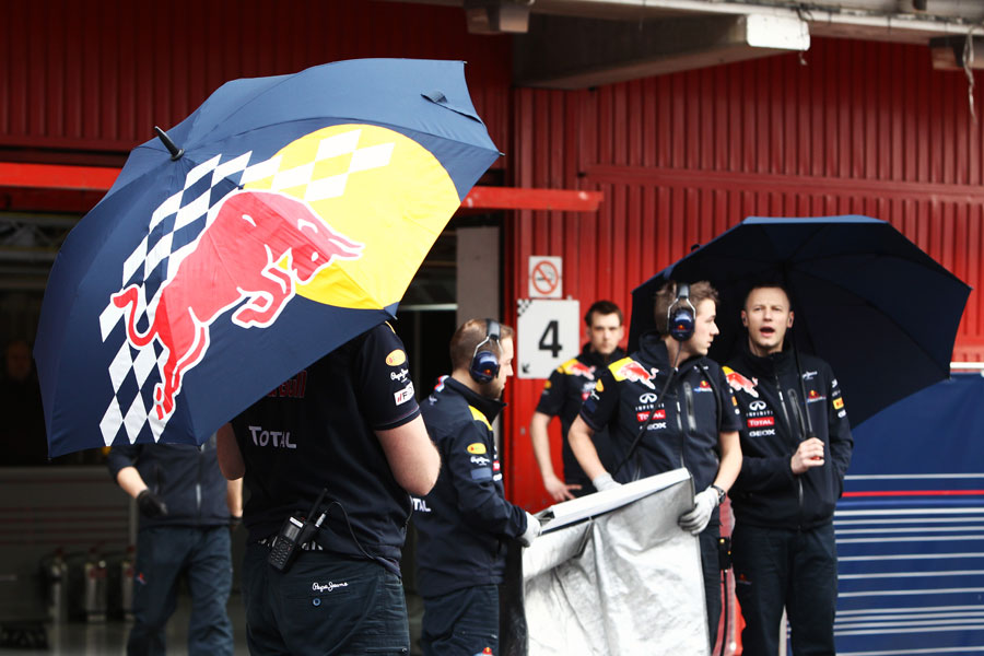 Red Bull mechanics with umbrellas wait for Sebastian Vettel to return