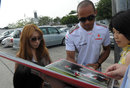 Lewis Hamilton signs a picture of himself driving in GP2 for fans in the paddock