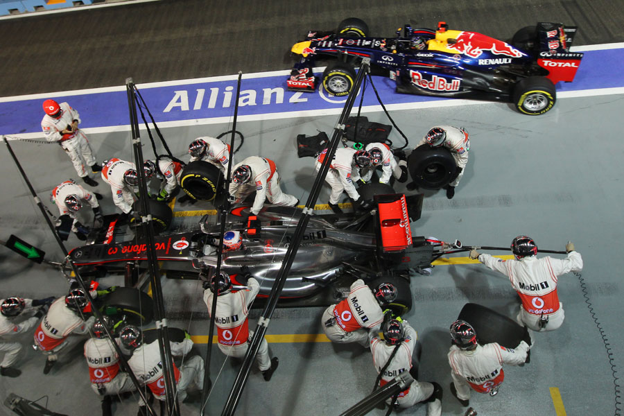 Jenson Button pits as Sebastian Vettel leaves his pit box