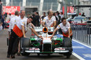 Force India mechanics wheel their car down the pit lane