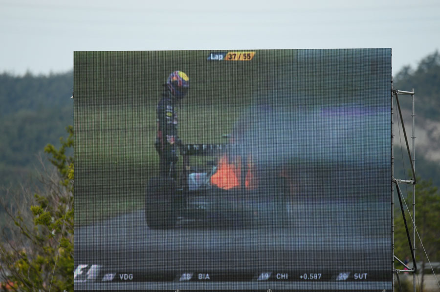 Mark Webber stares at the fire burning at the rear of his Red Bull