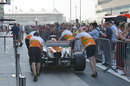 Force India wheels its car up the pit lane while fans watch on
