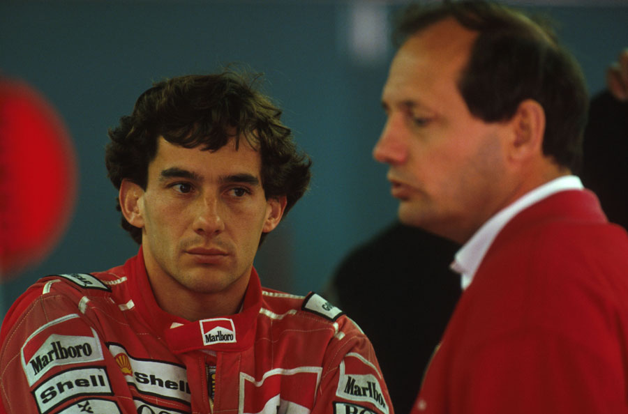 Ayrton Senna watches on as Ron Dennis talks in the paddock