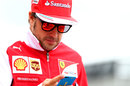 Fernando Alonso checks his phone as he walks through the paddock