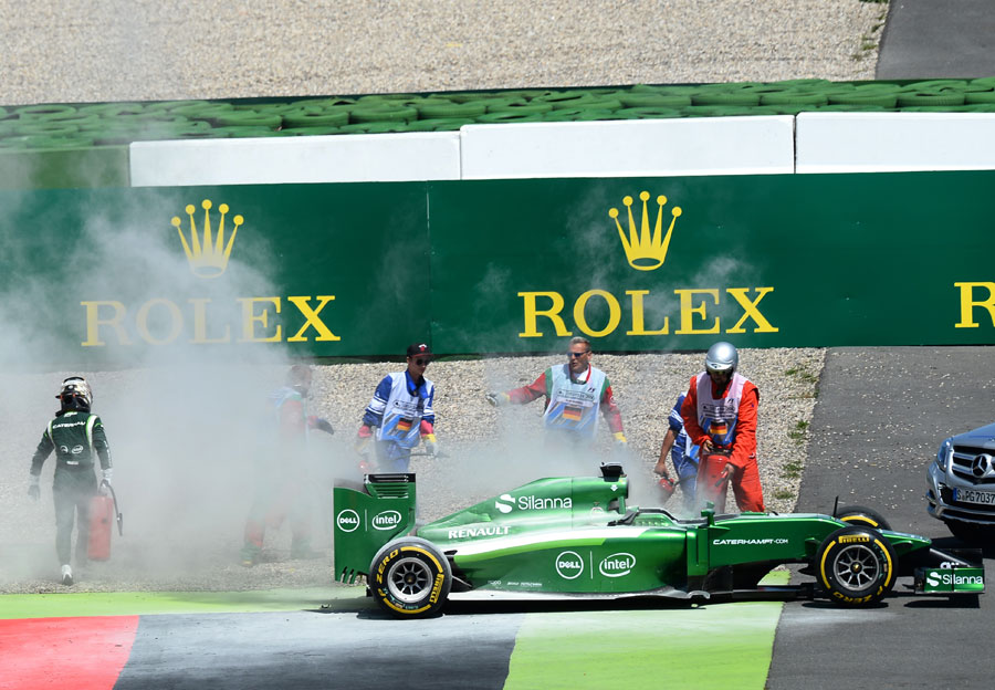 Kamui Kobayashi grabs a fire extinguisher to deal with his smoking Caterham