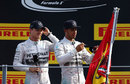 Nico Rosberg looks on as Lewis Hamilton signs a flag hoisted by fans beneath the podium