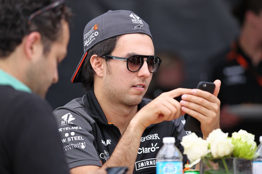 Sergio Perez checks his phone in the paddock