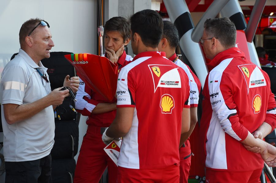 Ferrari mechanics talk to an FOM technician in the pit