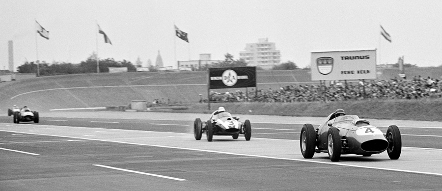 Tony Brooks, in the the Ferrari 246/F1, followed closely by the Cooper of Masten Gregory on the main straight