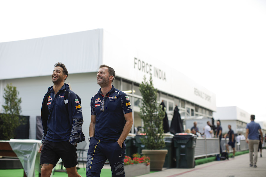 Daniel Ricciardo talks with his team member while walking through the paddock