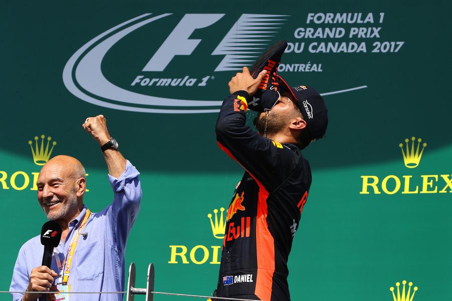 Daniel Ricciardo does a shoey on the podium watched by Patrick Stewart