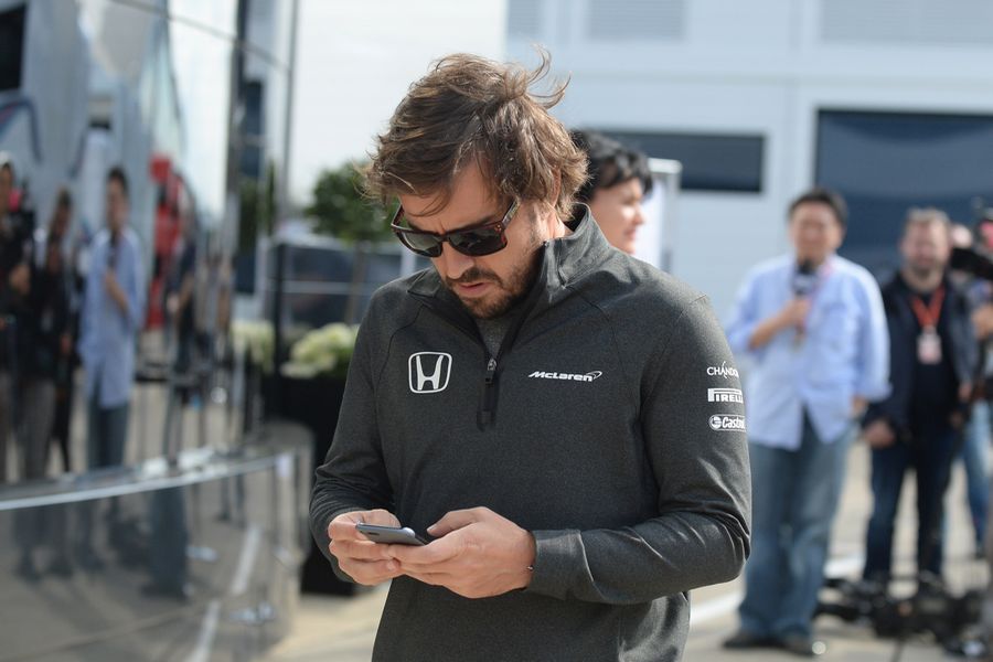 Fernando Alonso checks his phone in the paddock