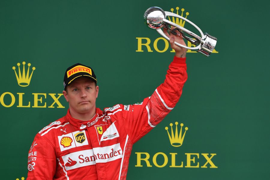 Kimi Raikkonen raises his winner's trophy on the podium as Felipe