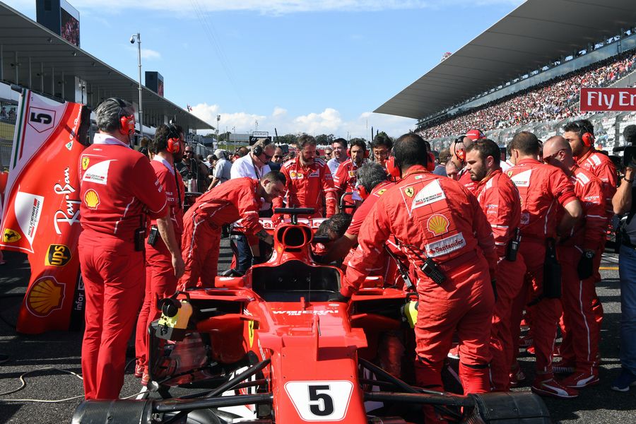 Ferrari mechanics observe the car of Sebastian Vettel on the grid with technical issues
