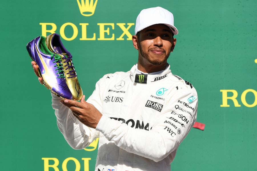 Race winner Lewis Hamilton celebrates on the podium with the running shoes of Usain Bolt