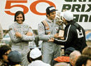 Emerson Fittipaldi looks on as Peter Revson is presented with the trophy