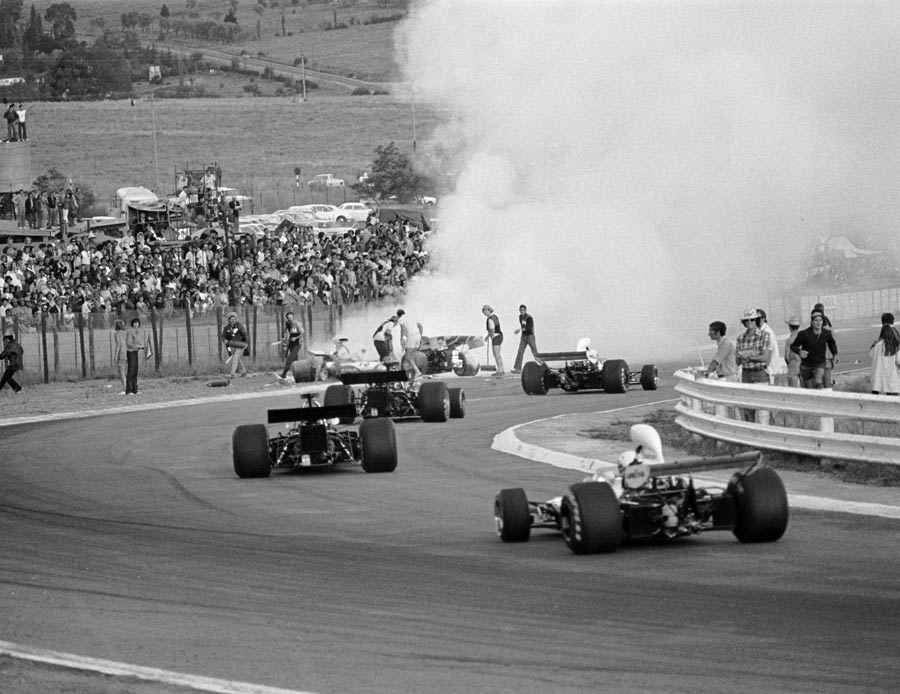 Cars stream past the fiery accident involving Mike Hailwood, Clay Regazzoni and Jacky Ickx