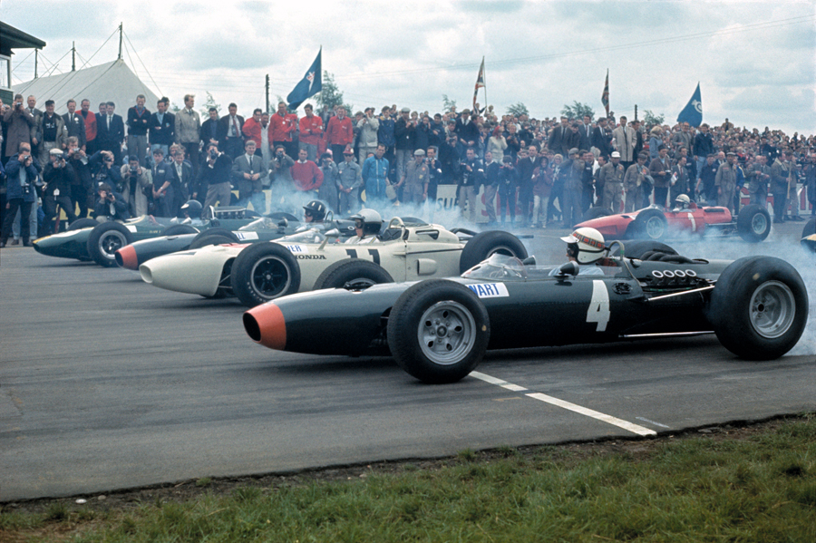 Tyre smoke fills the air as the field moves off with Jackie Stewart nearest the camera, then Richie Ginther and Jim Clark, with John Surtees in the second row