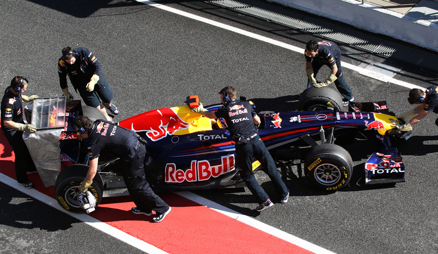 Red Bull crew push Sebastian Vettel back into the garage while covering up the rear of the car