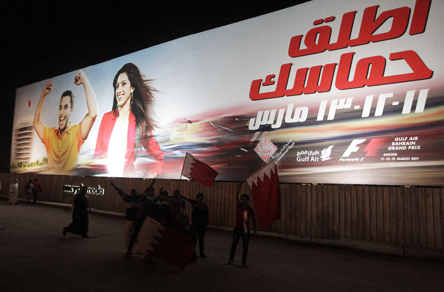 Protesters walk past a poster advertising the cancelled Bahrain Grand Prix, Manama