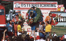 Carlos Reutemann stands on top of the podium with Denny Hulme to his right and James Hunt keeping the crowd entertained to his left